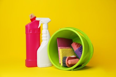 Green bucket, cleaning supplies and tools on yellow background