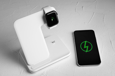 Smartwatch charging with wireless pad and mobile phone on white stone table
