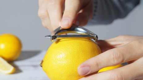 Photo of Man peeling lemon at table, closeup view