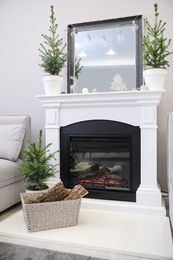 Little fir trees and Christmas decorations in room with fireplace. Stylish interior design