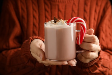 Woman holding glass cup of tasty cocoa with marshmallows and Christmas candy cane, closeup