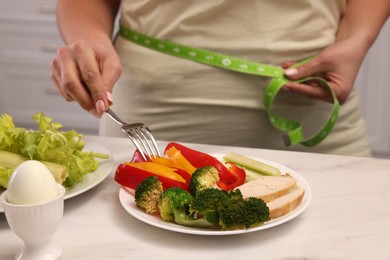 Overweight woman measuring waist while having meal at home, closeup