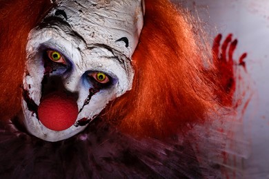 Photo of Terrifying clown against bloodstained plastic film, closeup. Halloween party costume