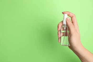 Woman holding antiseptic spray on green background, closeup. Space for text