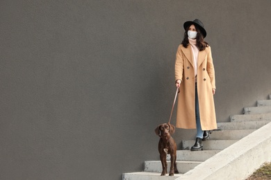 Photo of Woman in protective mask with German Shorthaired Pointer going downstairs outdoors. Walking dog during COVID-19 pandemic