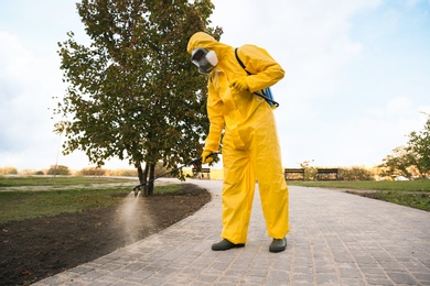 Person in hazmat suit disinfecting street pavement with sprayer. Surface treatment during coronavirus pandemic