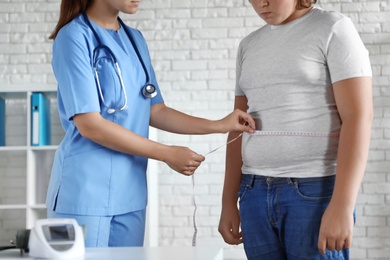 Female doctor measuring overweight boy in clinic, closeup view