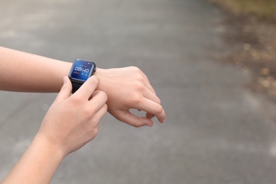 Woman using smart watch to check time or heart rate outdoors, closeup