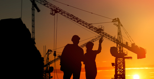 Silhouettes of engineers near construction site at sunrise