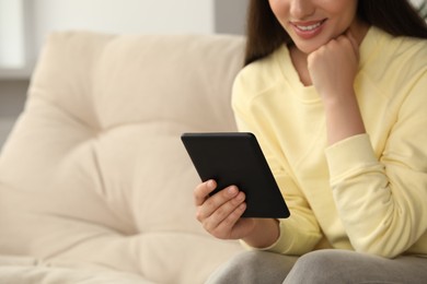 Young woman using e-book reader on sofa at home, closeup. Space for text