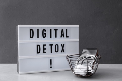 Trash bin of different gadgets and lightbox with words DIGITAL DETOX on light grey table