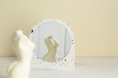 Beautiful female body shaped candle near mirror on white table