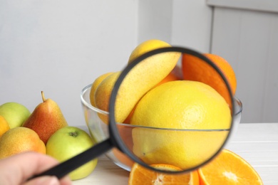 Woman with magnifying glass exploring lemons indoors, closeup. Poison detection