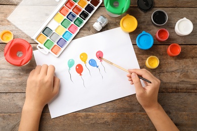 Girl painting picture of balloons on table, top view