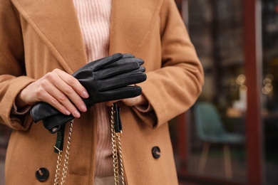 Young woman holding black leather gloves, closeup. Stylish clothes