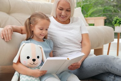 Photo of Happy grandmother with her granddaughter reading book together at home