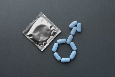 Photo of Male sign made of pills and condom on dark gray background, flat lay. Potency problem