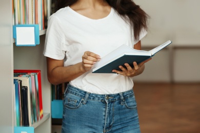 Young woman with book near shelving unit in library, closeup