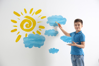 Little boy drawing sun and clouds on white wall 