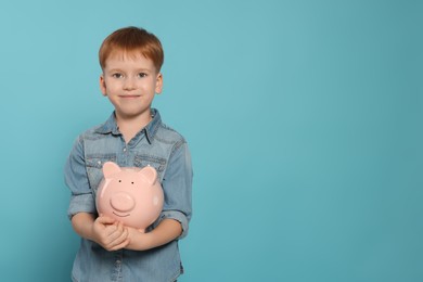 Cute little boy with ceramic piggy bank on light blue background, space for text