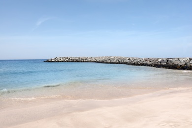 Picturesque view of beautiful beach with stone breakwater on sunny day