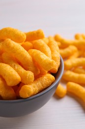 Many tasty cheesy corn puffs on white wooden table, closeup