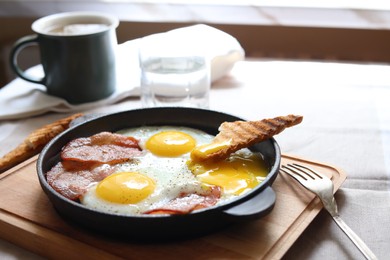 Tasty fried eggs with bacon and toast on table