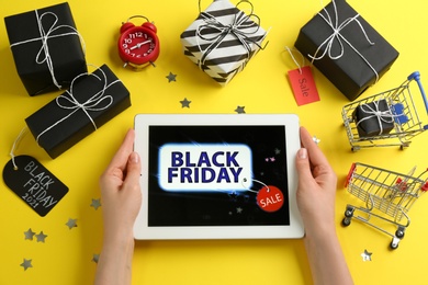 Woman with tablet surrounded by gifts on yellow background, top view. Black Friday sale