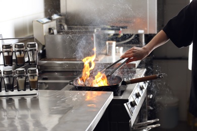 Female chef cooking meat with burning flame on stove in restaurant kitchen, closeup