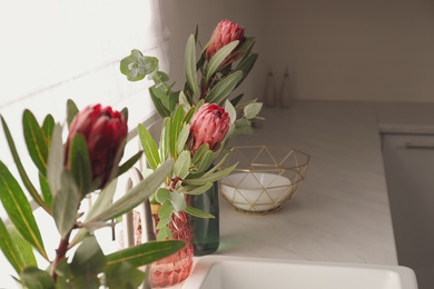 Photo of Beautiful protea flowers on countertop near window in kitchen, space for text. Interior design