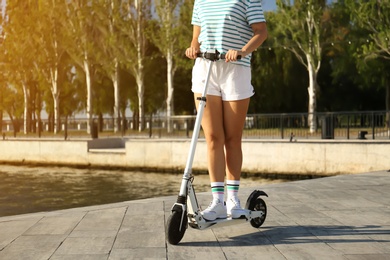 Young woman riding modern kick scooter along waterfront, closeup