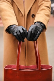 Young woman in black leather gloves holding red handbag, closeup. Stylish clothes