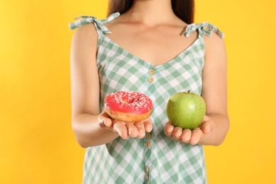 Concept of choice. Woman holding apple and doughnut on yellow background, closeup