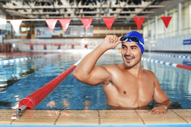 Photo of Young athletic man wearing cap and goggles in swimming pool