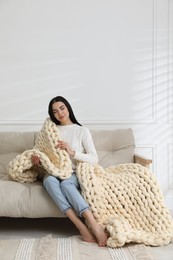 Young woman with chunky knit blanket on sofa at home