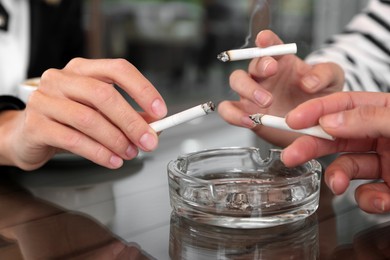Women holding cigarette over glass ashtray at table, closeup