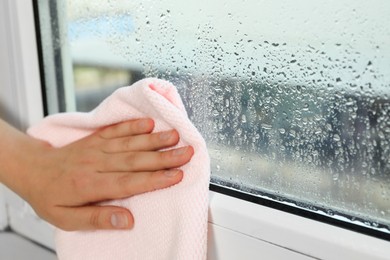 Woman wiping window glass with drops of condensate indoors, closeup. Space for text