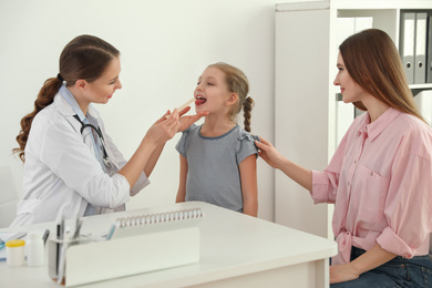 Mother and daughter visiting pediatrician. Doctor examining little patient's throat in hospital