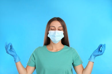 Woman in protective mask meditating on light blue background. Dealing with stress caused by COVID‑19 pandemic