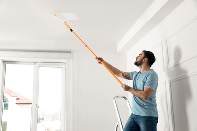 Photo of Young man painting ceiling with white dye indoors