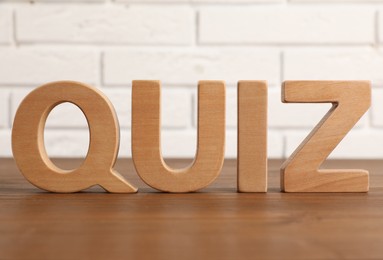 Word Quiz made with wooden letters on table near white brick wall