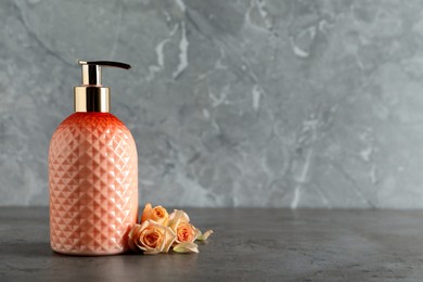 Stylish dispenser with liquid soap and beautiful flowers on grey table, space for text