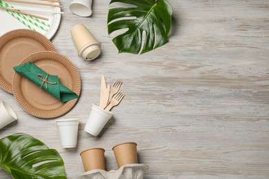 Flat lay composition with disposable tableware and monstera leaves on white wooden background. Space for text