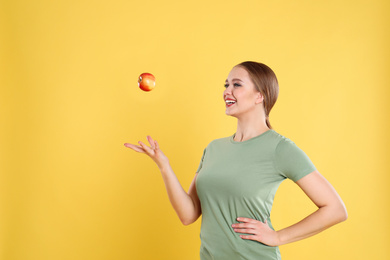 Young woman with apple on yellow background. Vitamin rich food
