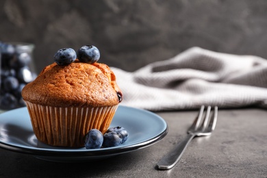 Photo of Plate with tasty muffin and blueberries on grey table. Space for text