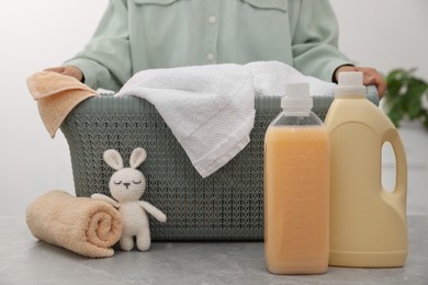Photo of Woman holding basket with towels and bottles of laundry detergents indoors, closeup