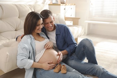 Photo of Young pregnant woman and her husband with baby's shoes at home