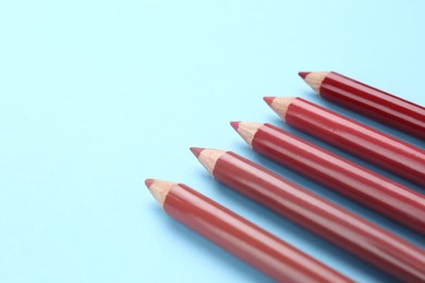 Different lip pencils on light blue background, closeup view with space for text. Cosmetic product