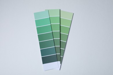 Photo of Color paint chips of green shades on light background, top view