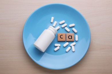 Wooden cubes with symbol Ca (Calcium), medical bottle and pills on light blue plate, top view